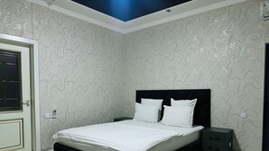 A bedroom with a bed, a bedside table, a rug, and patterned wallpaper. - ALI HOTEL (Namangan)