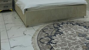 A bedroom with a large bed, a nightstand, a decorative wall panel, and a patterned rug. - ALI HOTEL (Namangan)