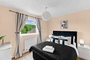 Ein Schlafzimmer mit Bett, Nachttisch, Vorhängen am Fenster, Heizkörper und Deckenleuchte.