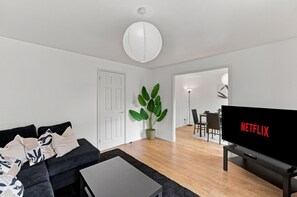 Un saló modern amb un sofà, una taula de centre, una planta en test i una zona de dinar amb cadires, i un televisor que mostra el logotip de Netflix.