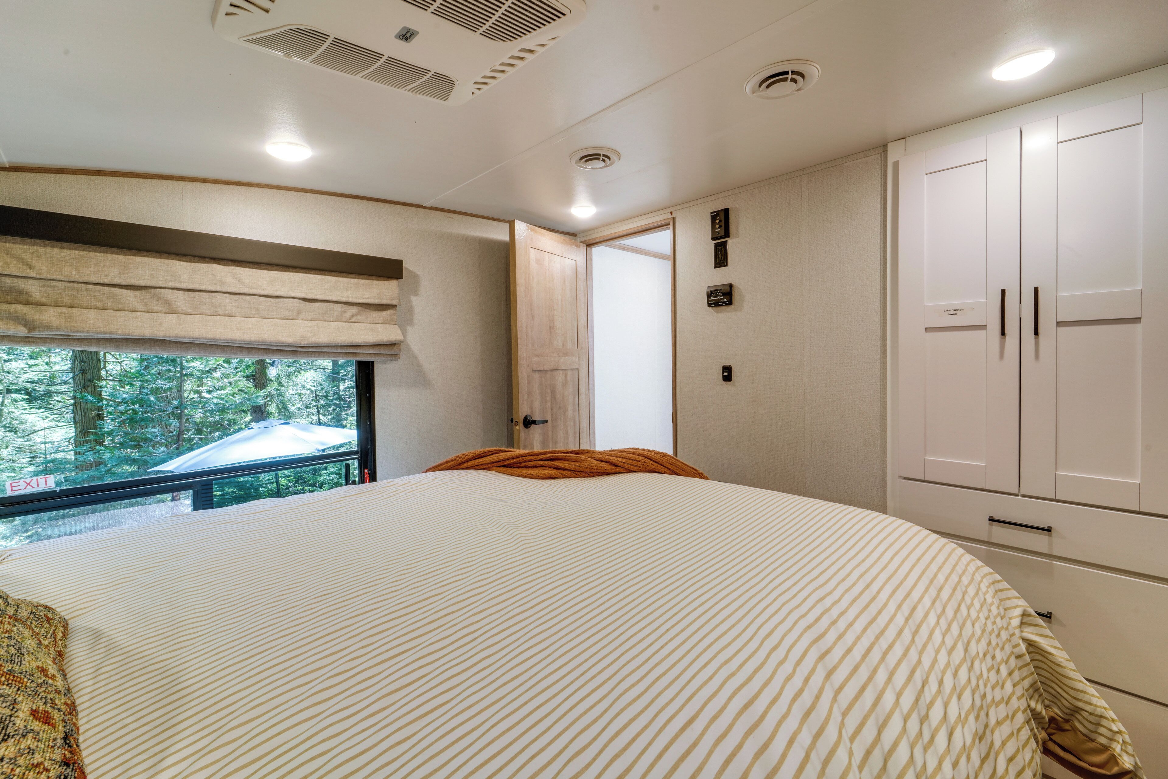 A bedroom with a large bed, a window with an 'EXIT' sign, a wardrobe, and a door leading outside.