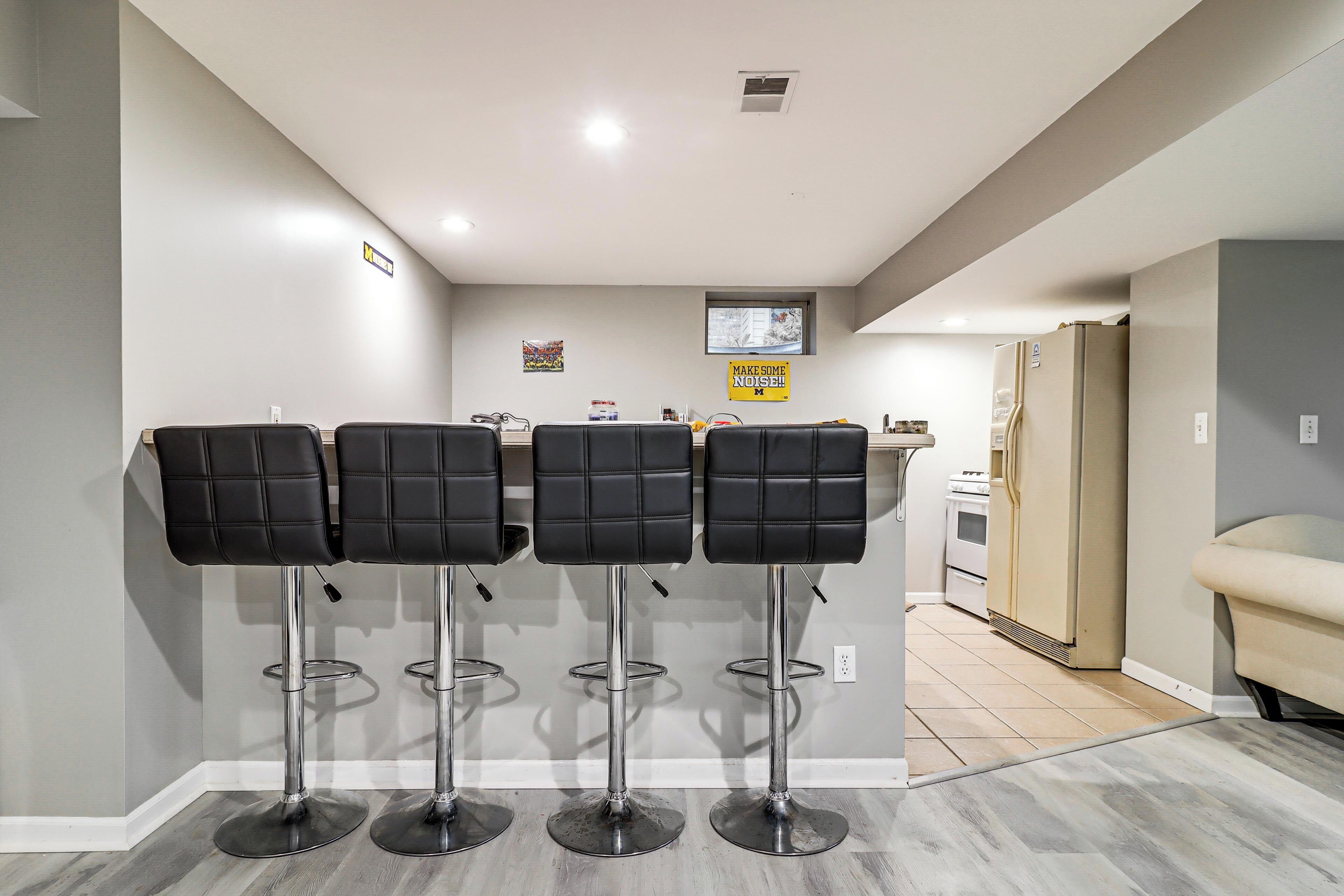 A kitchen area with a bar stool setup, a refrigerator, and a sink.
