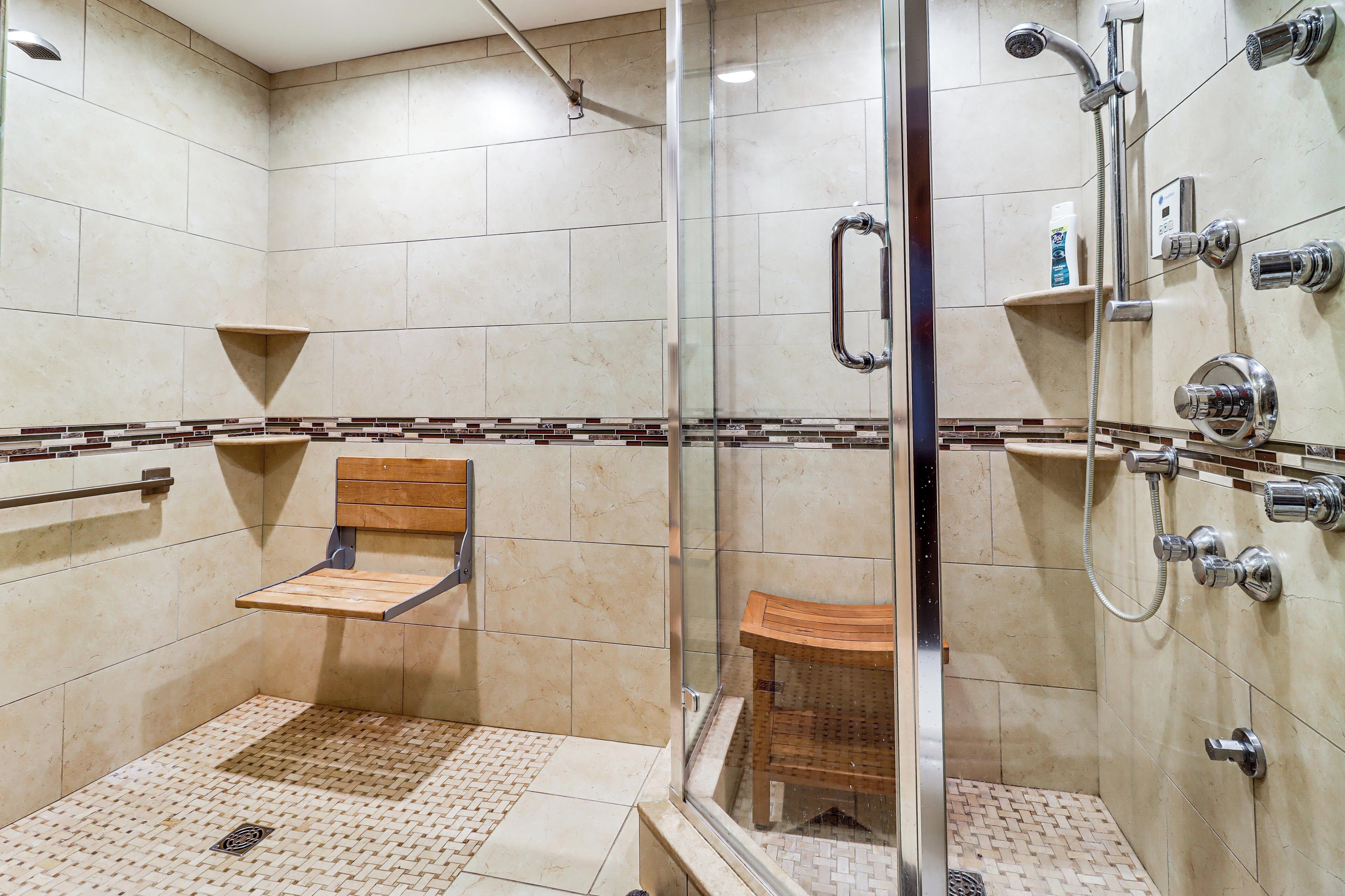 A glass-enclosed shower area with a wooden chair, a shelf with toiletries, and a tiled floor.