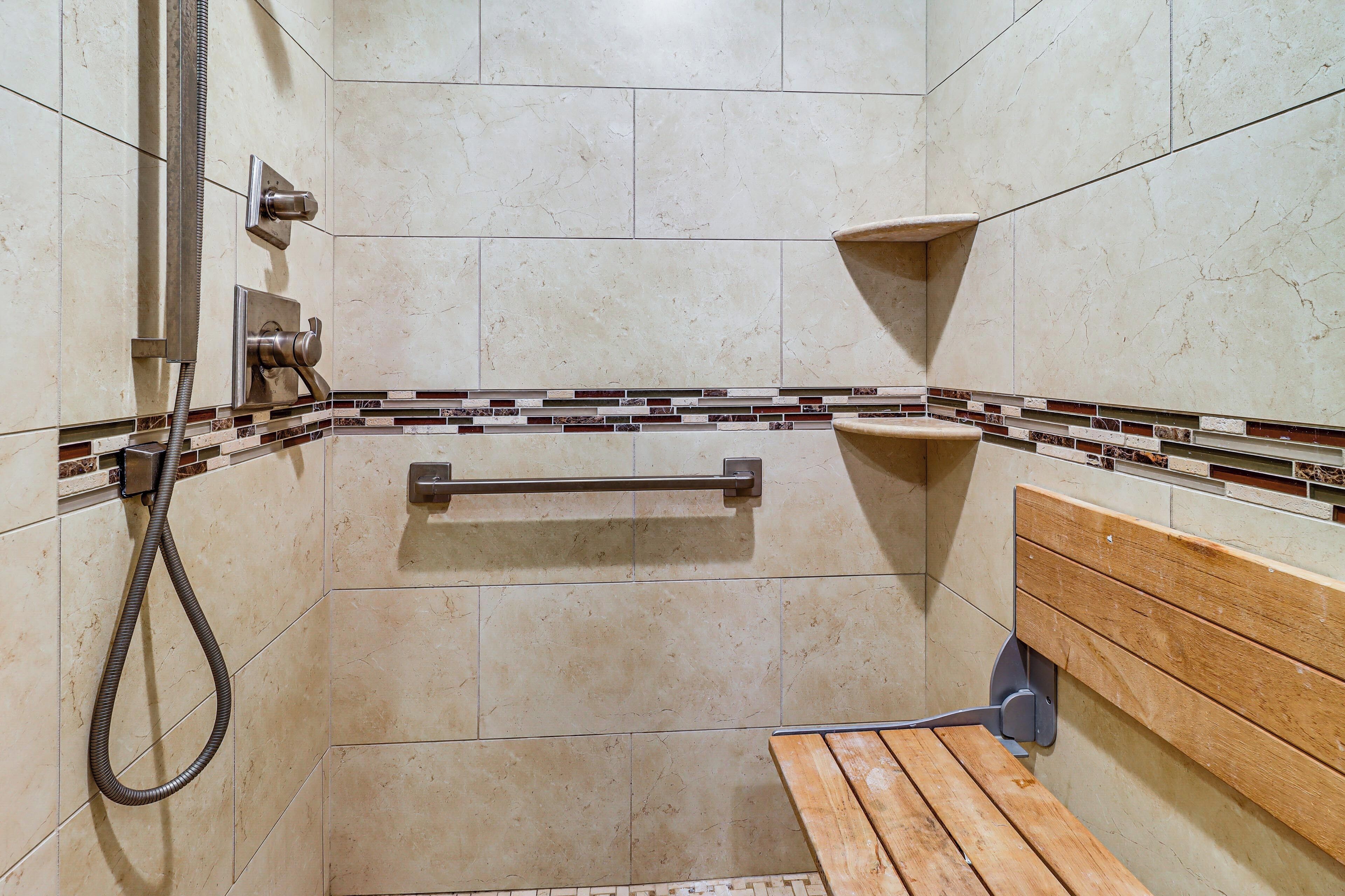 Eine Dusche mit Duschbrause, einer Holzbank und einer gefliesten Wand mit dekorativer Bordüre.