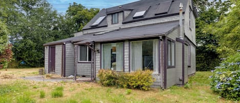 Ein zweistöckiges Haus mit geneigtem Dach, großen Fenstern und einer Veranda.
