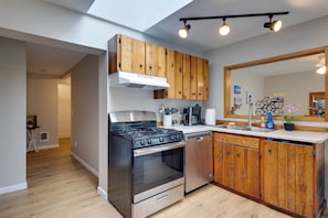 A modern kitchen with wooden cabinets, stainless steel appliances, and a skylight.