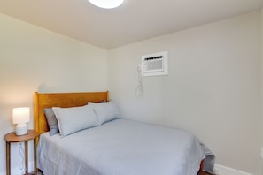 A bedroom with a bed, a bedside table with a lamp, a wall-mounted air conditioning unit, and a power outlet. - Deck & Dock Access! Sunlit Lake Livingston Escape (Pointblank)