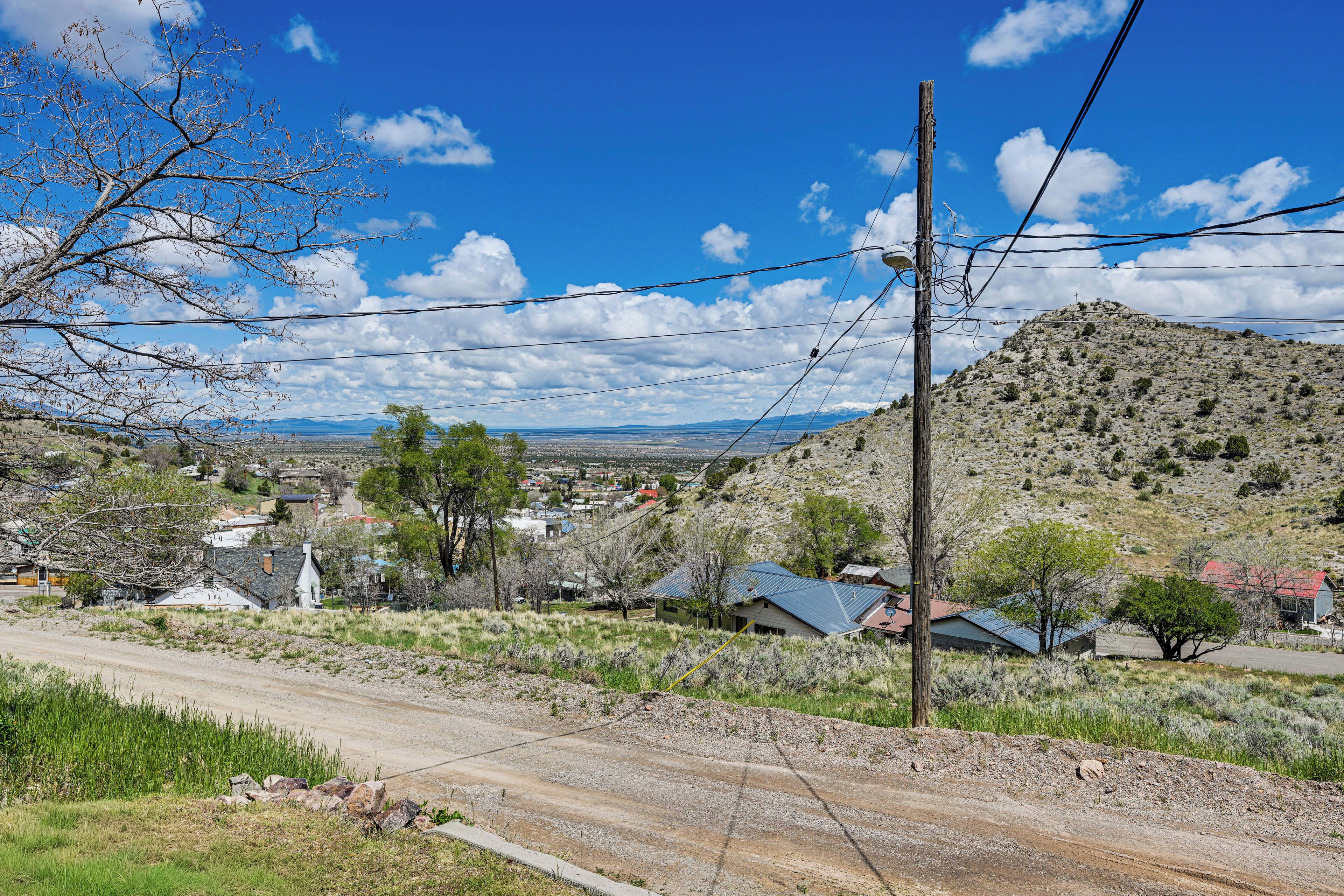 Paisaje rural con un camino de tierra, casas y una colina al fondo.