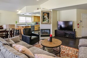 A living room with a sofa, a coffee table, a TV, a fireplace, and a kitchen in the background. - Pets Welcome! Yucca Valley Haven w/ Fenced Yard (Yucca Valley)