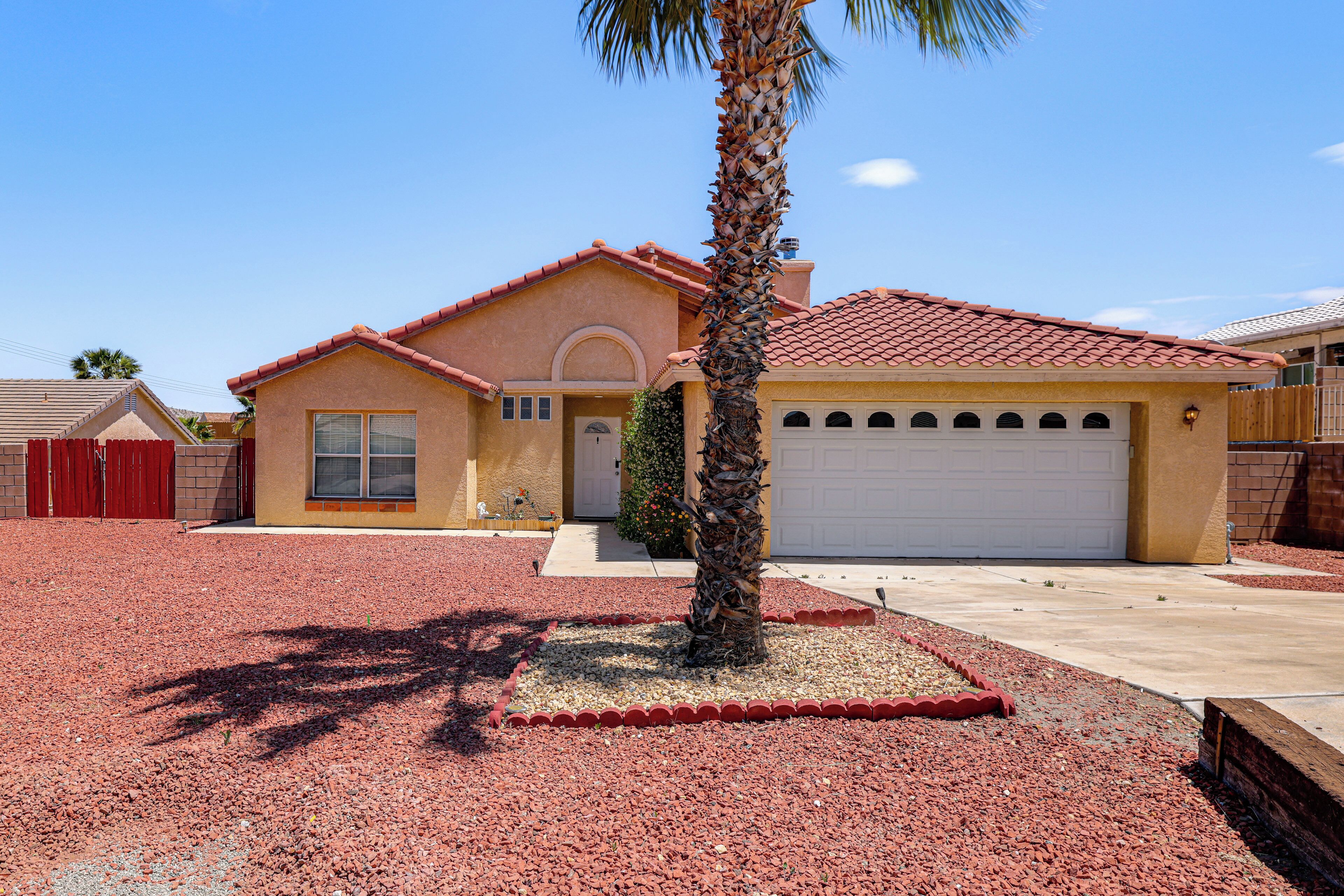 A residential house with a red-tiled roof, a garage, and a palm tree in the front yard.