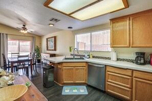 A kitchen with wooden cabinets, a dishwasher, a coffee maker, and a dining area with a table and chairs. - Pets Welcome! Yucca Valley Haven w/ Fenced Yard (Yucca Valley)