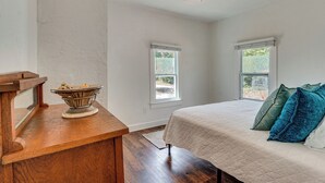 A bedroom with a bed, a wooden nightstand, a ceiling fan, and two windows.
