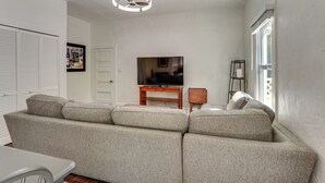 A living room with a sectional sofa, a television on a wooden stand, a ceiling fan, and a window with blinds.