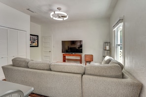 A living room with a sectional sofa, a television on a wooden stand, a ceiling fan, and a window with blinds.