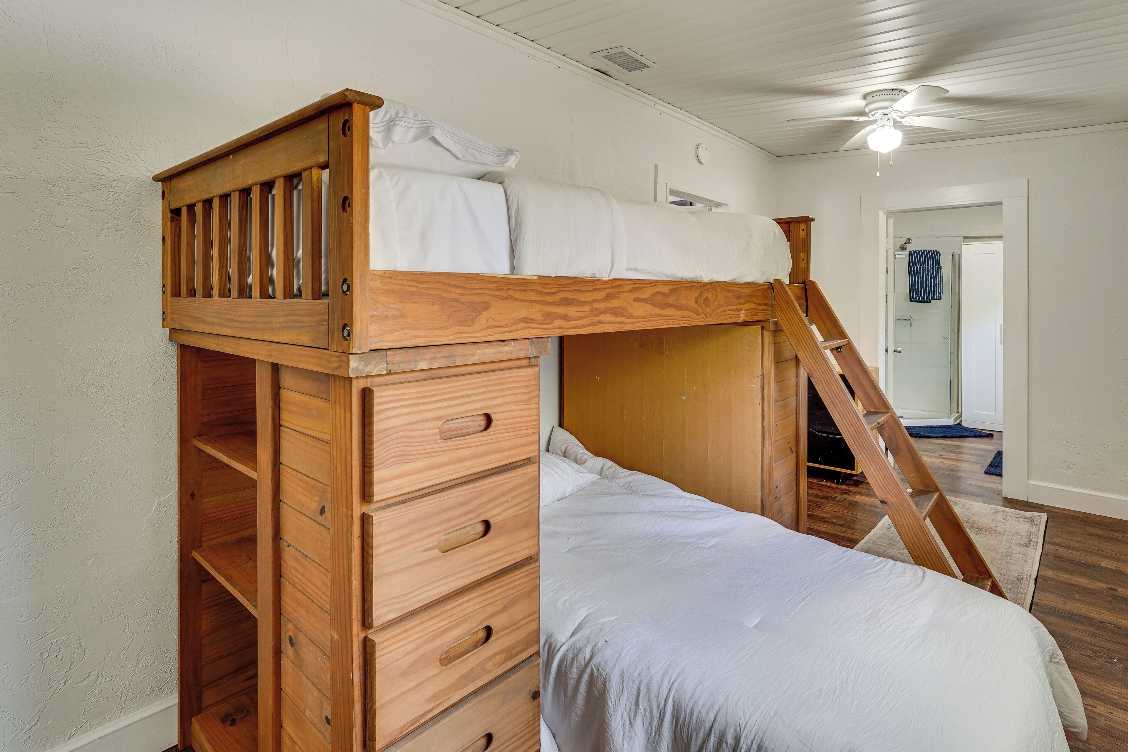Ein Stockbett mit Holzleiter, eine Holzkommode mit Schubladen und ein Deckenventilator.
