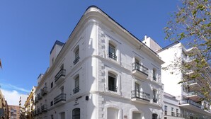Ein weißes Gebäude mit mehreren Balkonen und bogenförmigen Fenstern, das an einer Straßenecke steht.