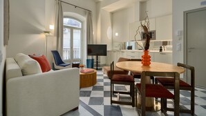 Ein modernes Wohnzimmer mit Sofa, Esstisch mit Stühlen, Fernseher und einer Küche im Hintergrund.