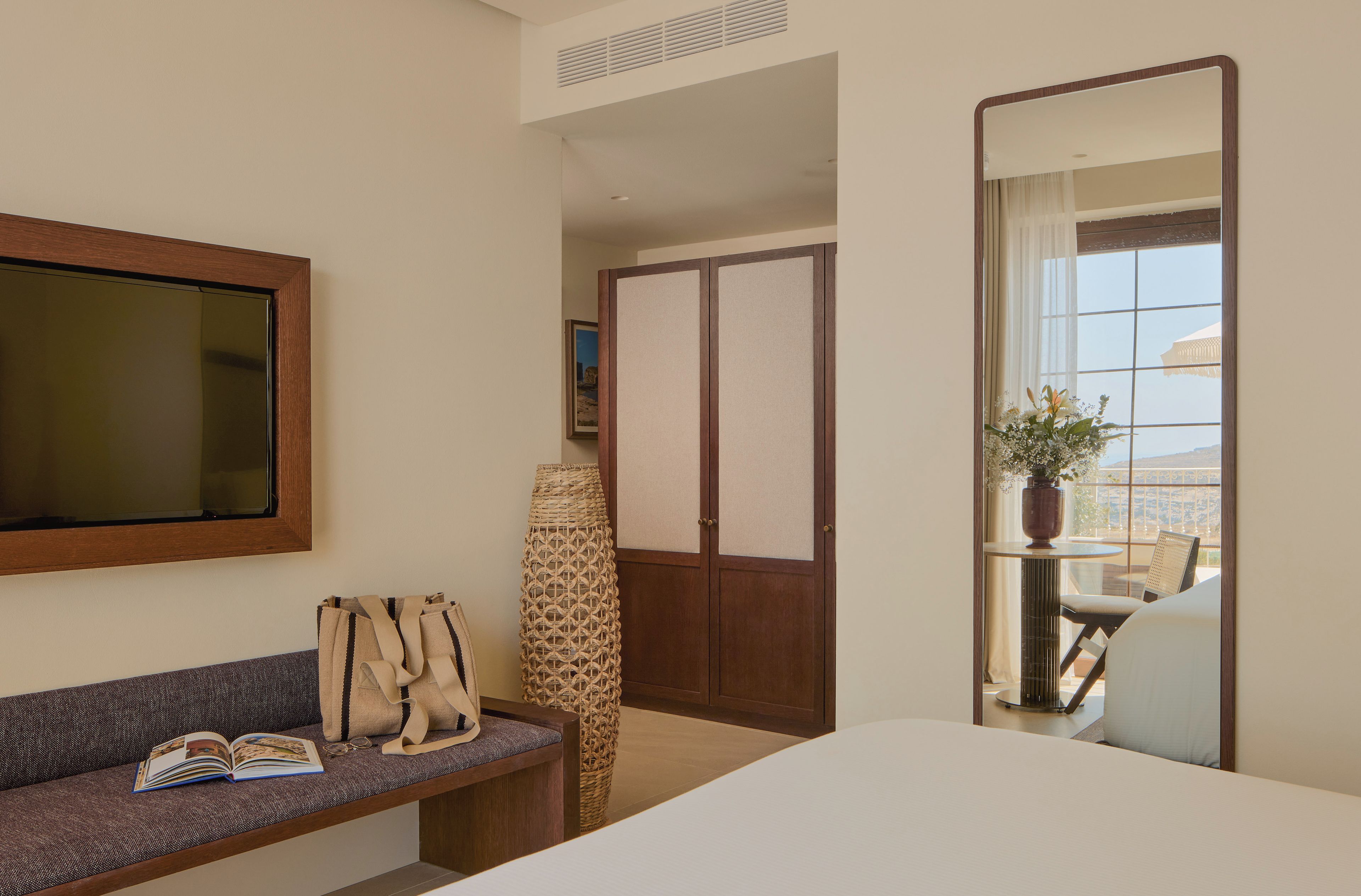 Habitación de hotel con cama, sofá, espejo, ventana con vistas y una mesita con una planta.