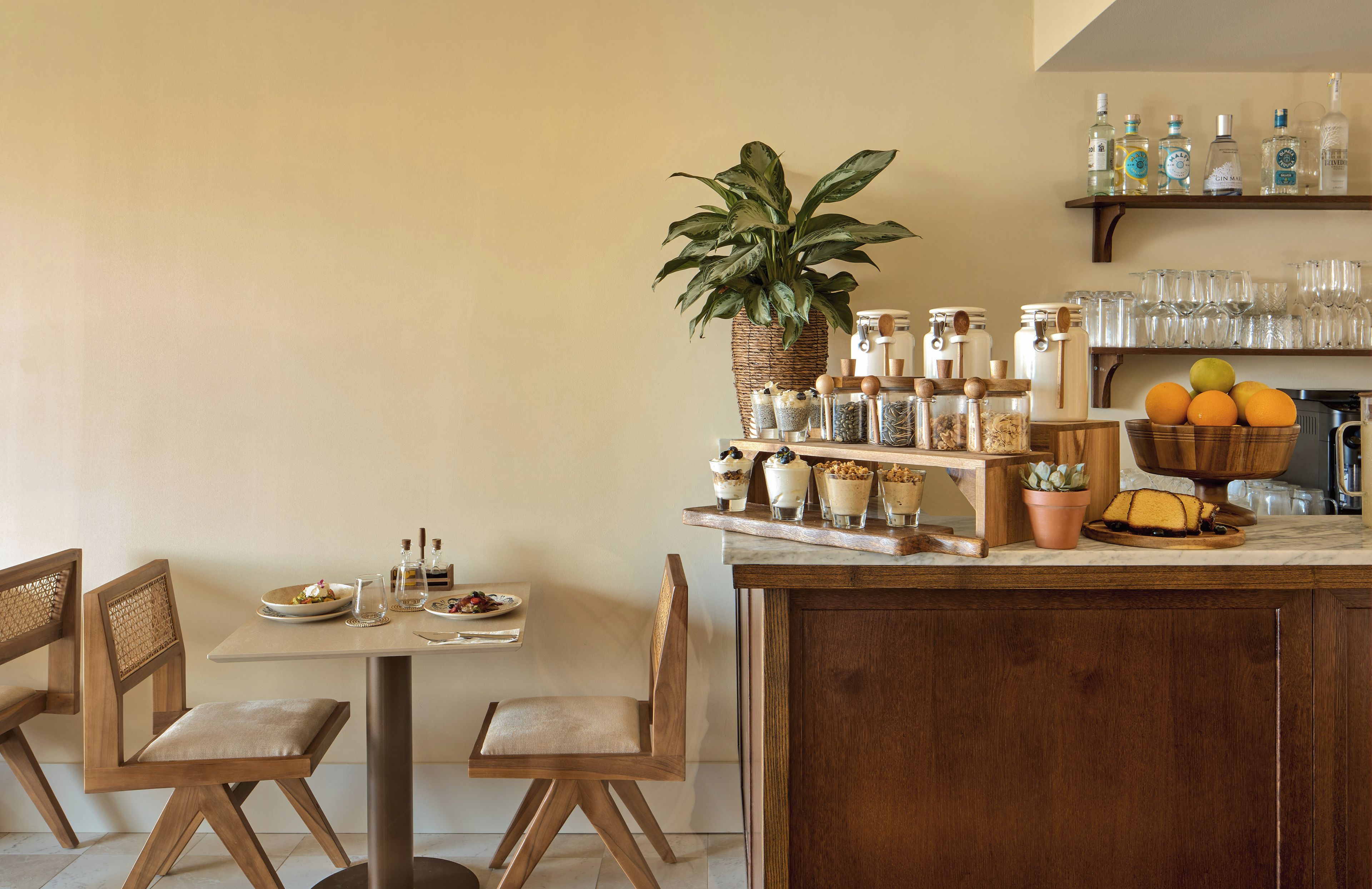 A dining area with a wooden table, chairs, a bar area with shelves of bottles, and a potted plant.