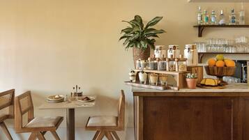 A dining area with a wooden table, chairs, a bar area with shelves of bottles, and a potted plant.