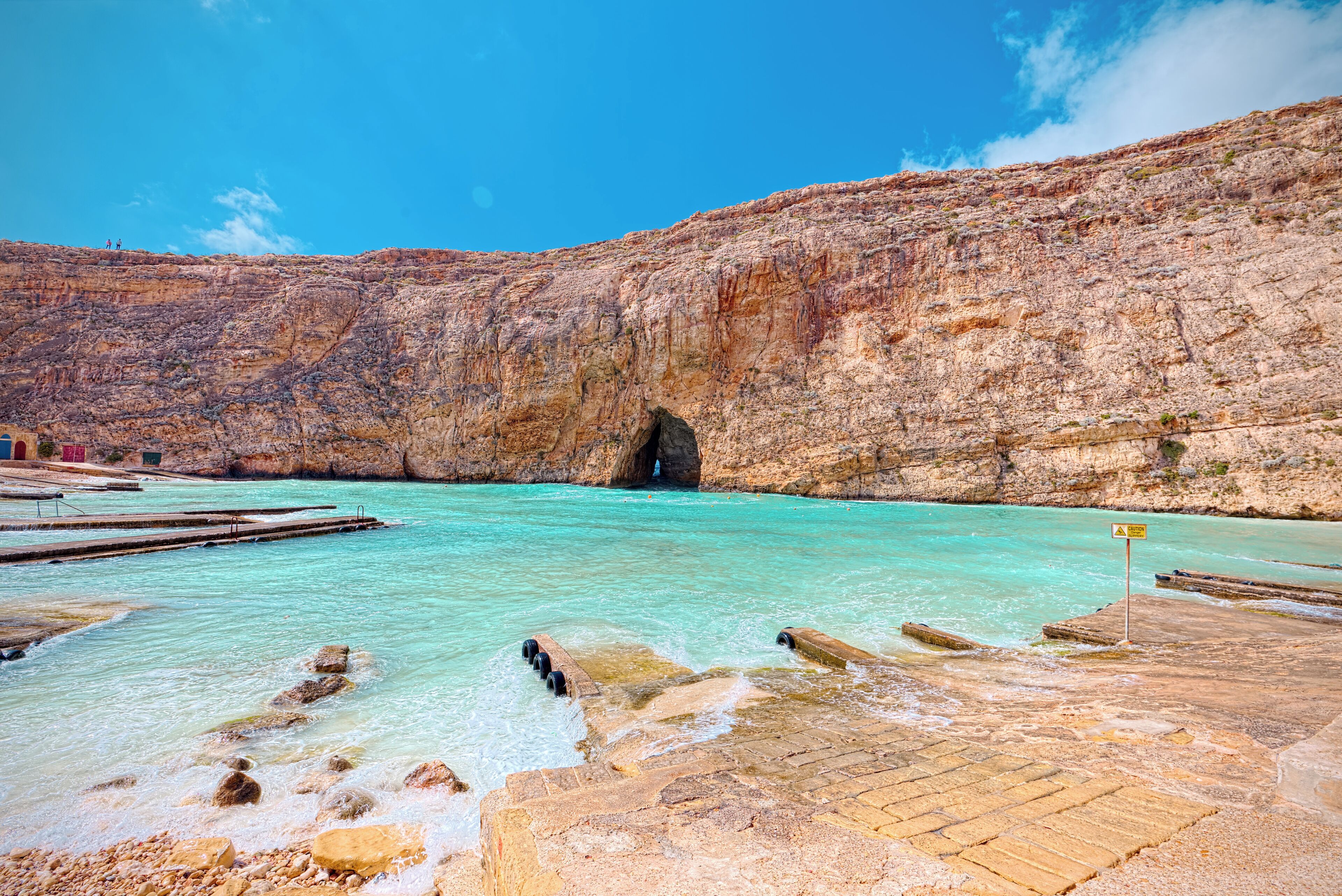 A natural pool with clear turquoise water, a rocky cliff, and a wooden dock.