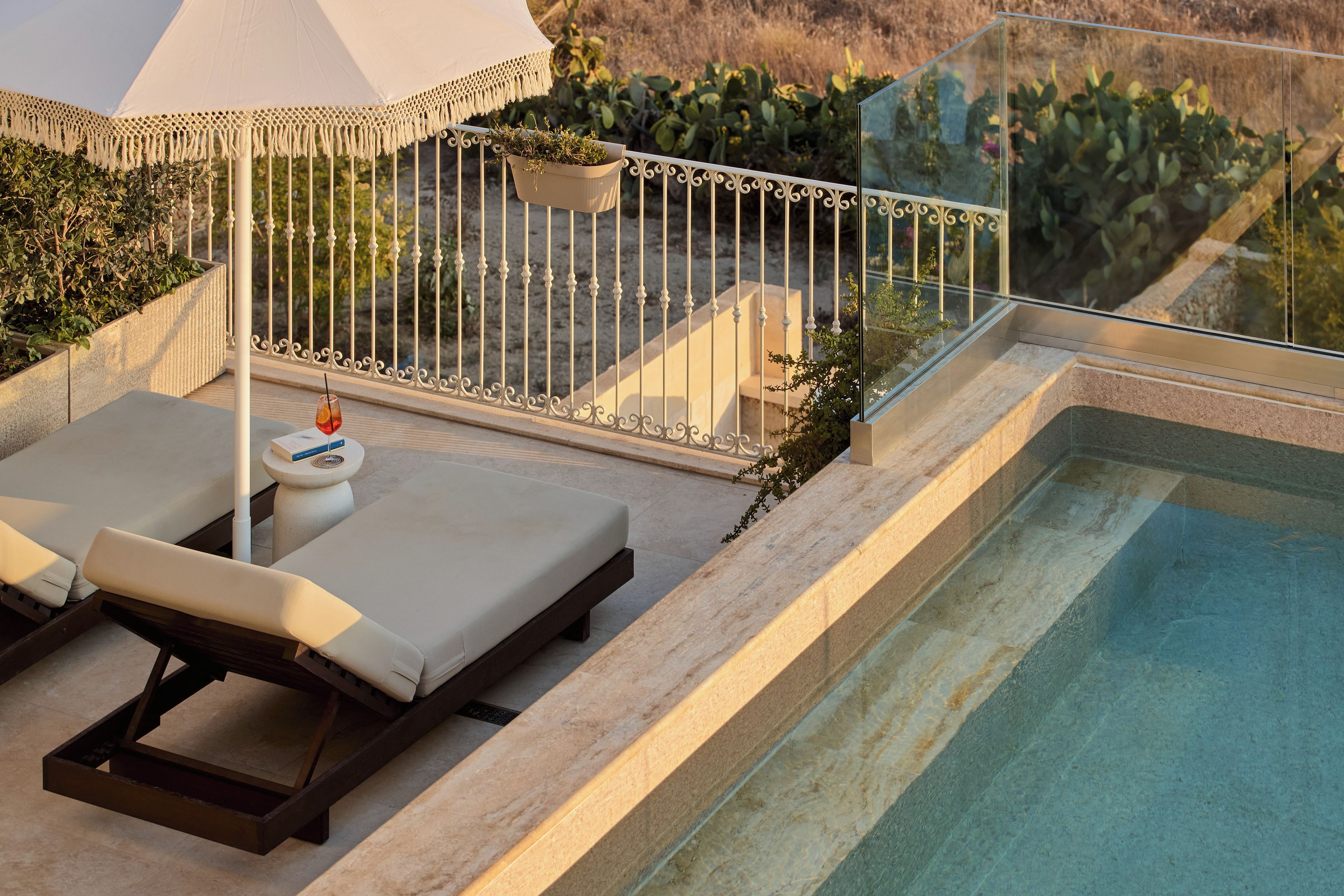 Un área de piscina en la azotea con sillones, una mesita con una bebida y un vaso de refresco.