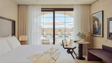 Habitación de hotel con una cama grande, un escritorio, una silla y vistas a una piscina y un edificio a través de la ventana.