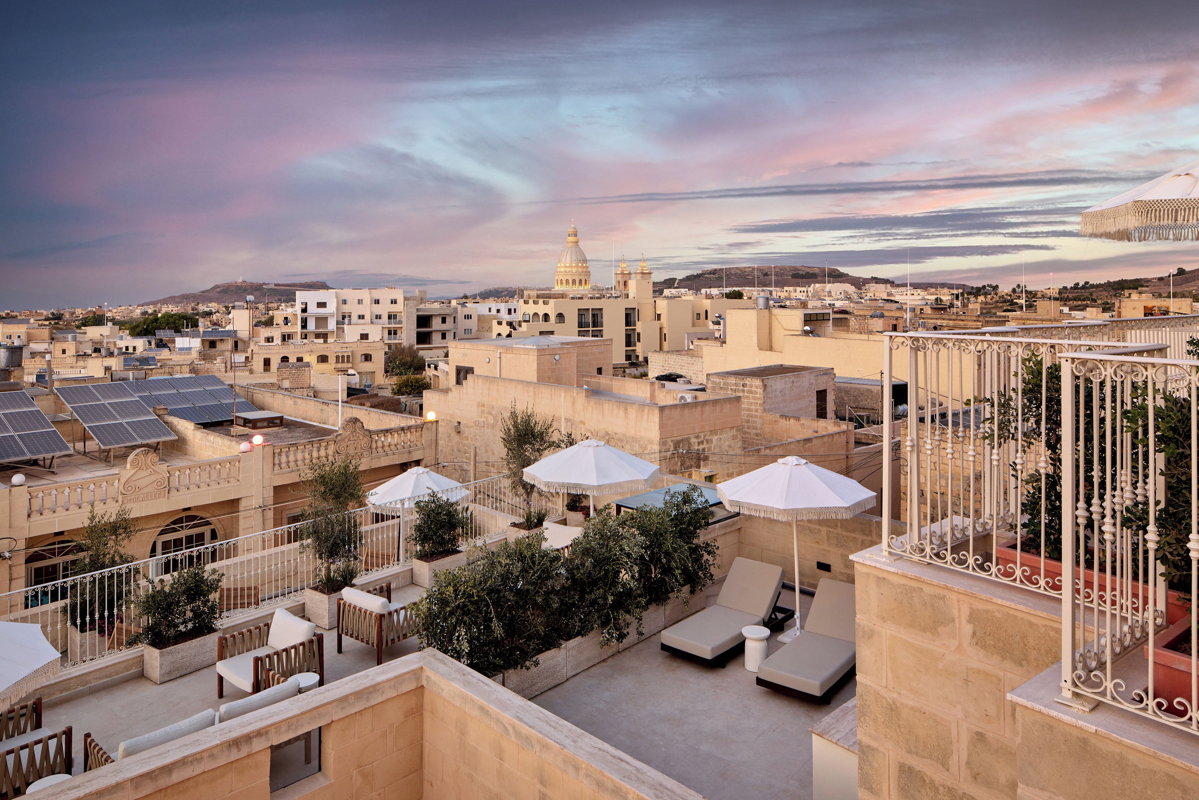A rooftop terrace with lounge chairs, umbrellas, and solar panels.