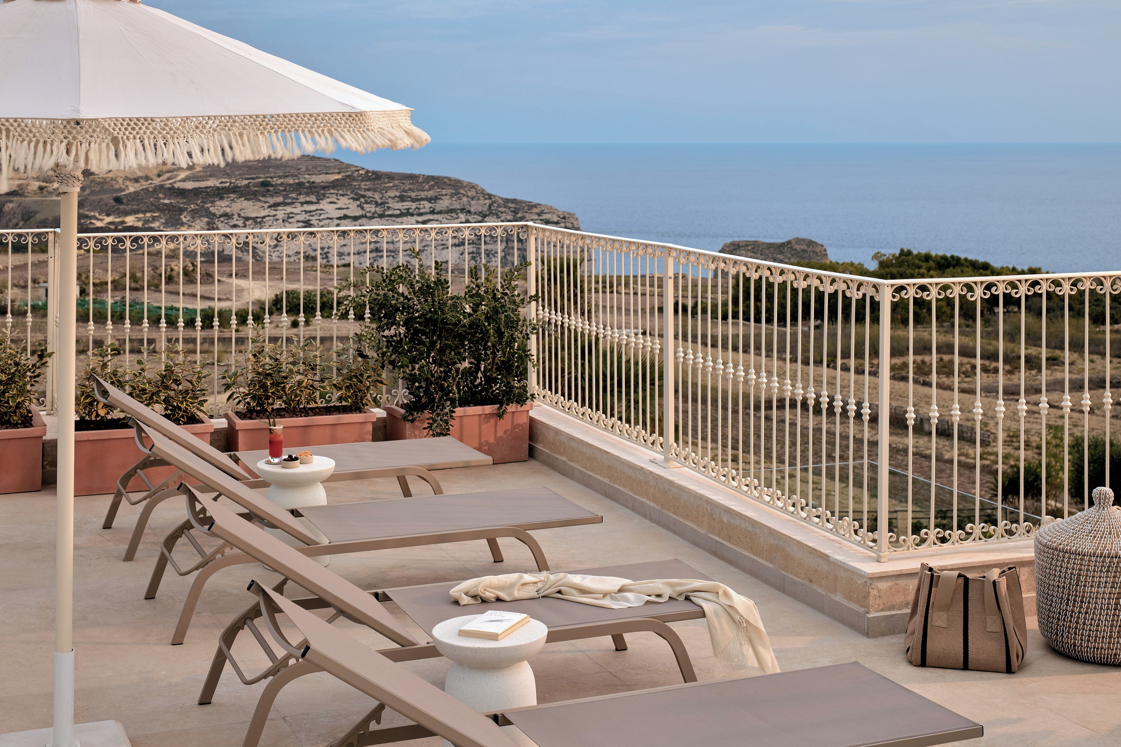 A terrace with lounge chairs, a table, and a view of the sea.