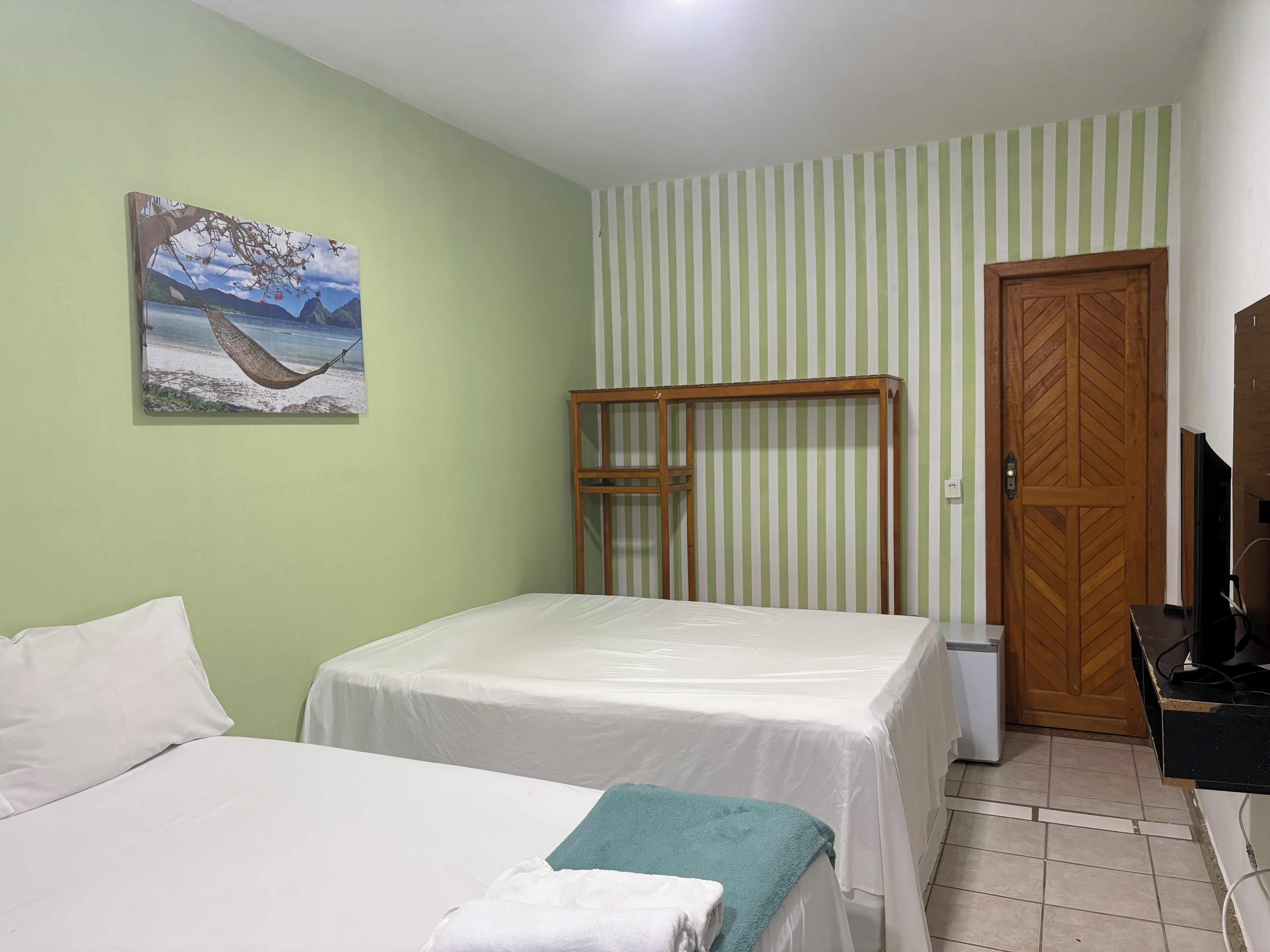 A room with two beds, a wooden bench, a door, and a painting on the wall.