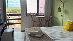 Quarto com cama, escrivaninha, cadeira, mesa pequena e janela com vista.