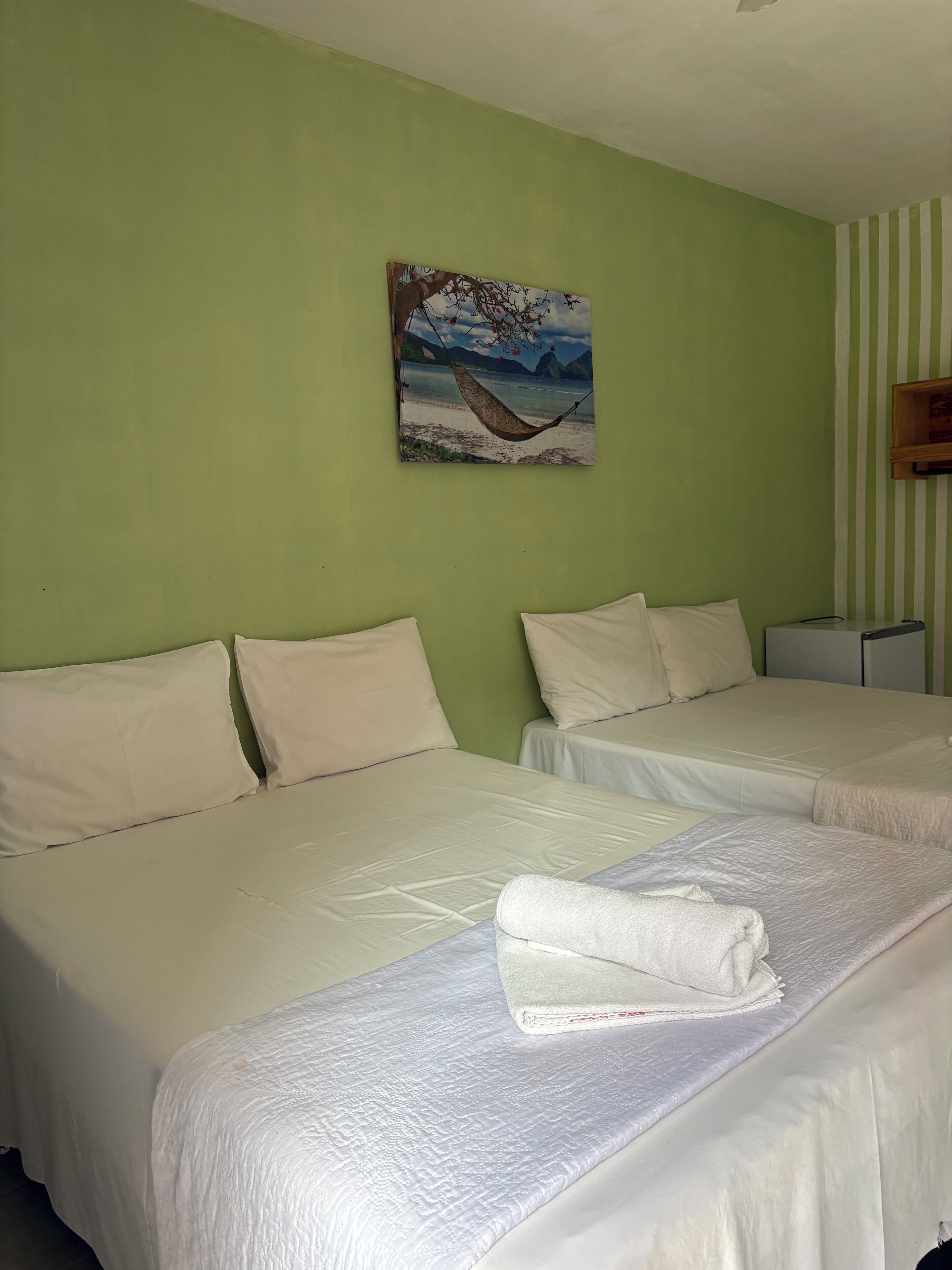 A hotel room with two beds, a painting of a beach scene, and a striped wall.