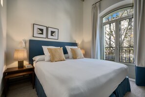 A neatly made bed with a blue headboard, two bedside lamps, and framed artwork on the wall. - Bright apartment with balcony in the heart of Seville (Seville)