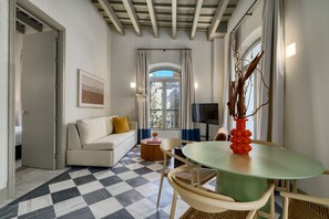 A room with a checkered floor, a sofa, a table with chairs, a TV, and a window with curtains. - Bright apartment with balcony in the heart of Seville (Seville)