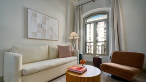 A living room with a sofa, a round coffee table, and a chair. There is a window with curtains, a lamp, and a framed picture on the wall. - Luis de Vargas 2B by Home at Homes (Seville)