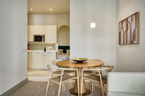 Une cuisine moderne avec des meubles blancs, un four à micro-ondes et un coin repas comprenant une table ronde en bois et des chaises en osier.