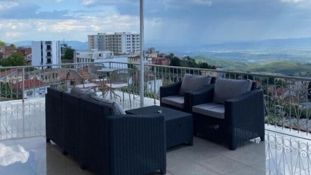 A balcony with outdoor furniture, a large umbrella, and a city view. - Villa Duka (Kruje)