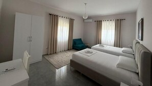 A modern hotel room with two beds, a desk, a chair, and a small seating area. - Villa Duka (Kruje)