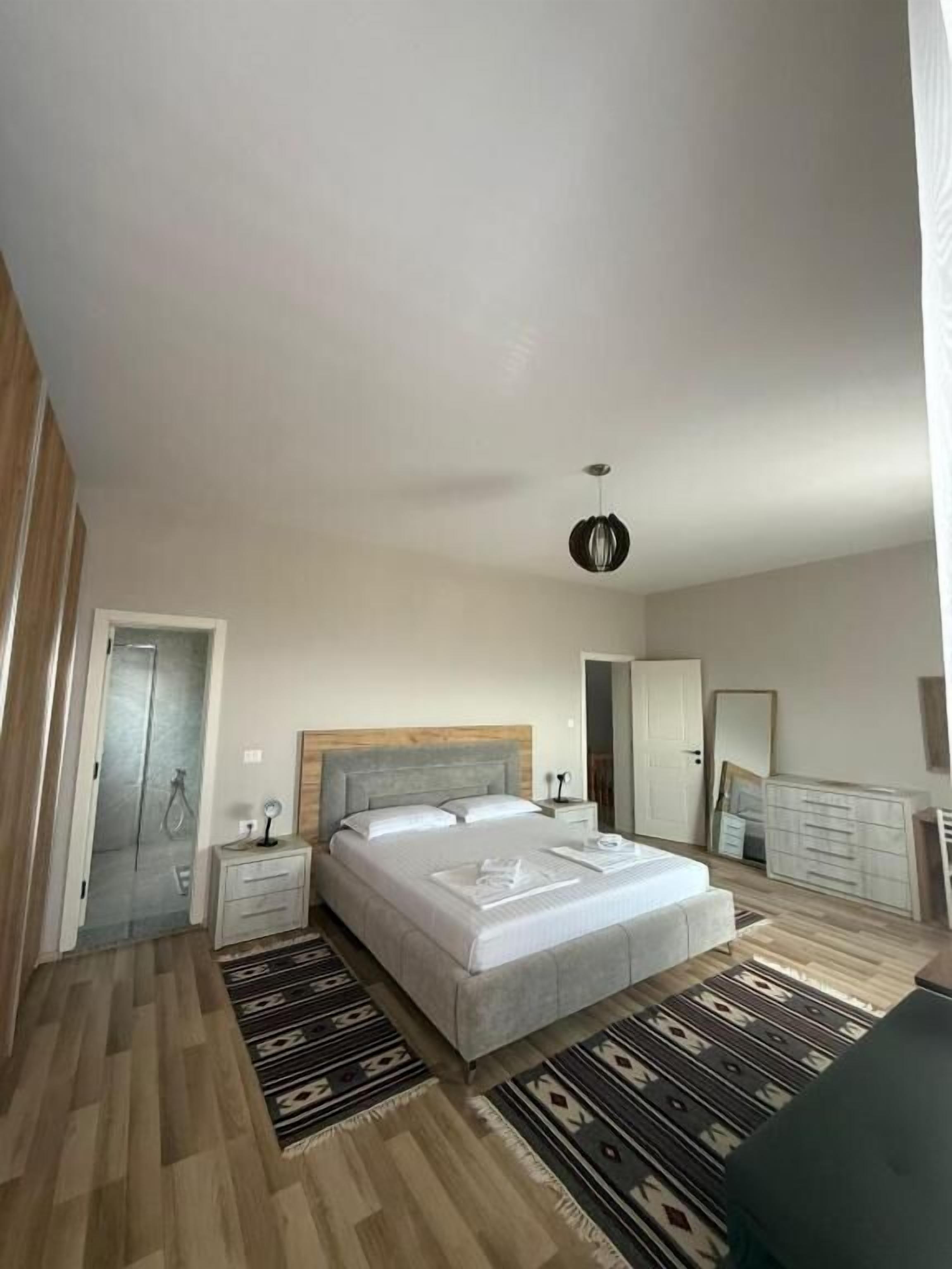 Une chambre à coucher comprenant un lit, des tables de chevet, une commode, un miroir, une armoire et une douche.