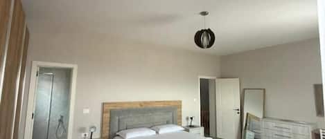 A bedroom with a bed, bedside tables, a nightstand, a mirror, a wardrobe, and a shower.