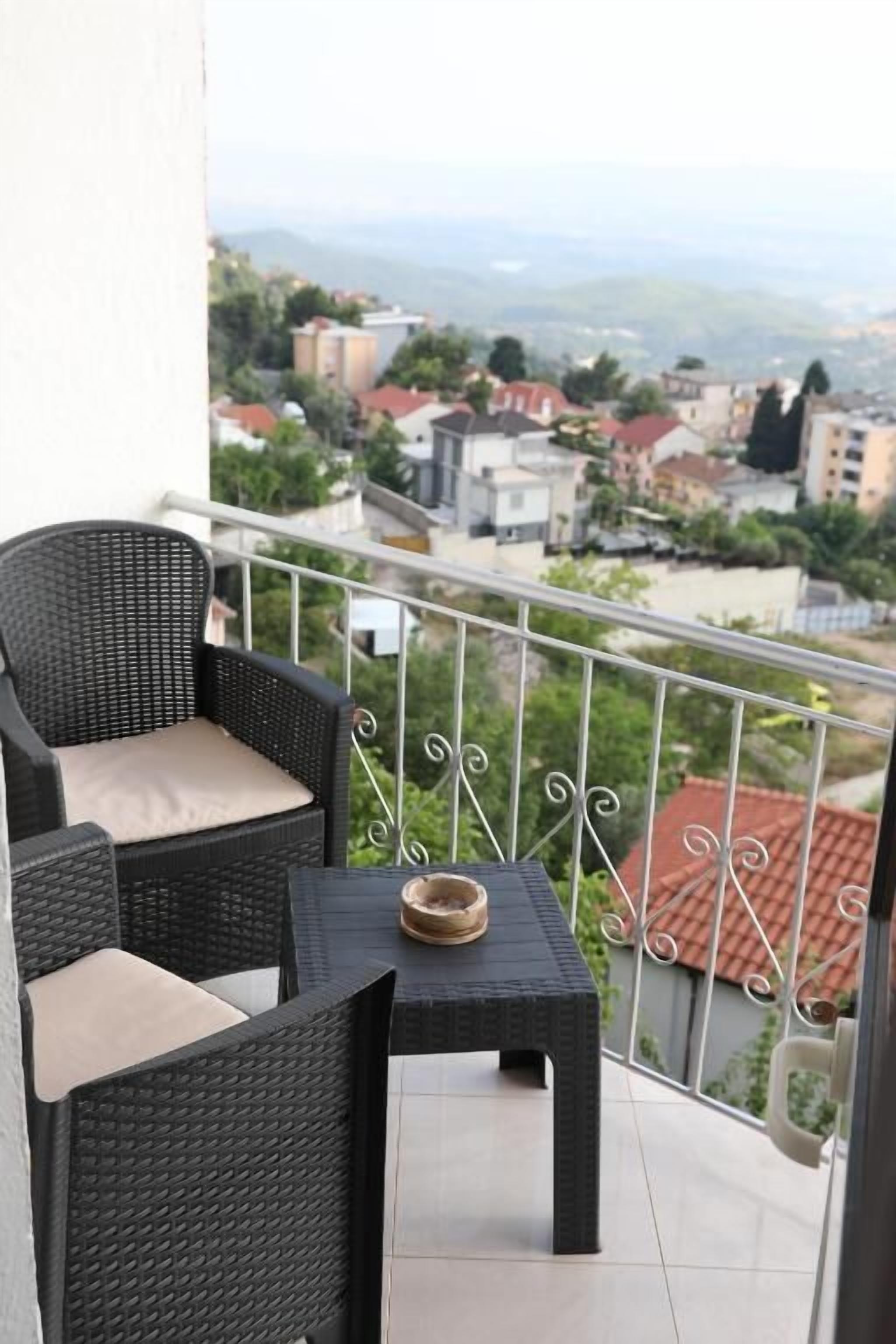 Un balcón con mobiliario de mimbre, una pequeña mesa y vistas a una zona residencial.
