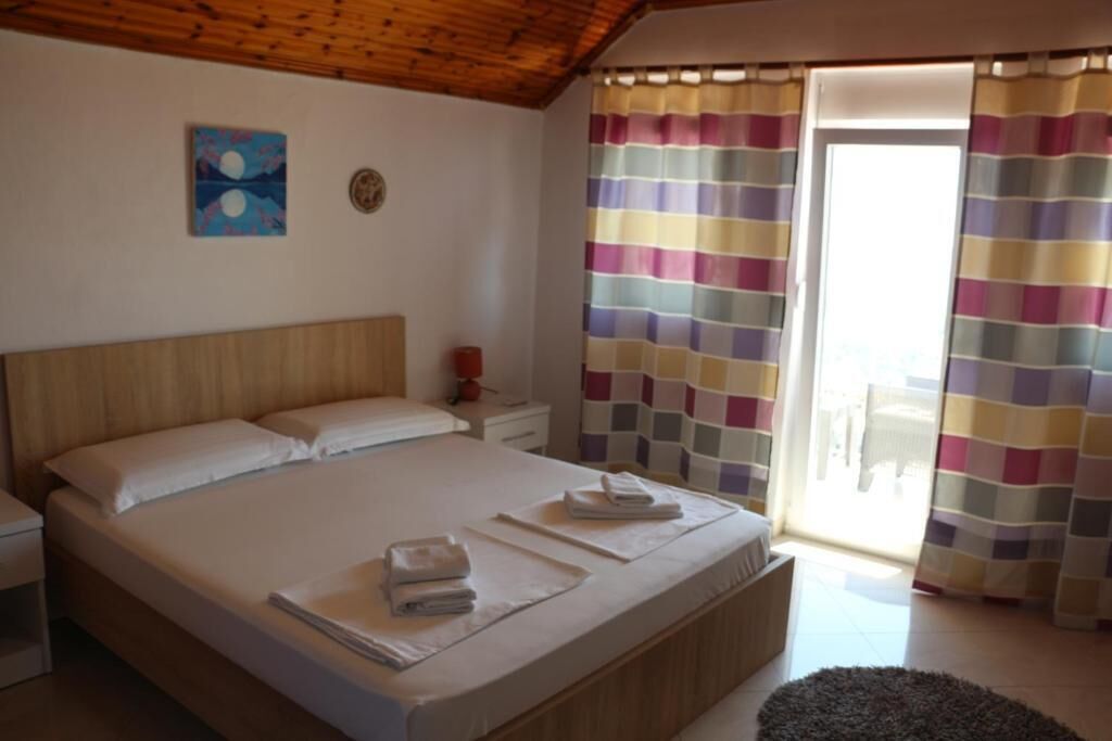 Un dormitorio con cama, mesitas de noche, un cuadro y vistas a través de una ventana con cortinas.