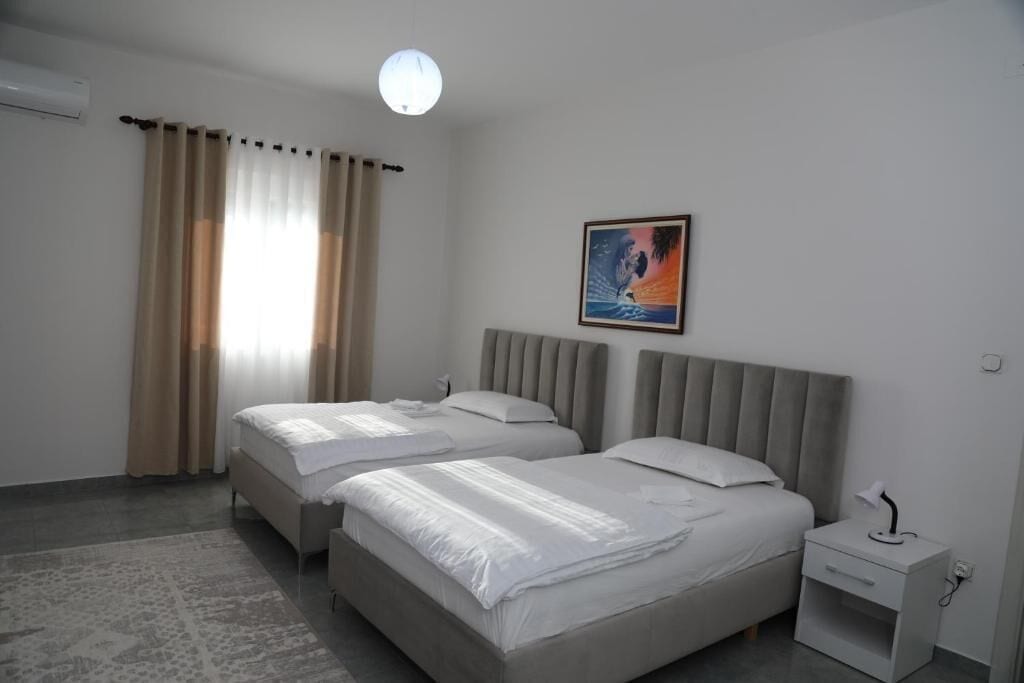 Una habitación de hotel con dos camas, una mesita de noche, un cuadro y una ventana con cortinas.
