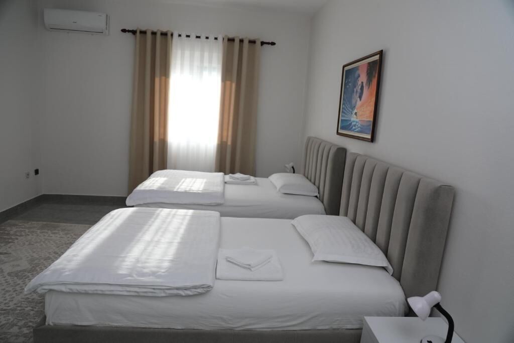 Ein Hotelzimmer mit zwei Betten, einem Heizkörper, einem Bild an der Wand und einem Fenster mit Vorhängen.