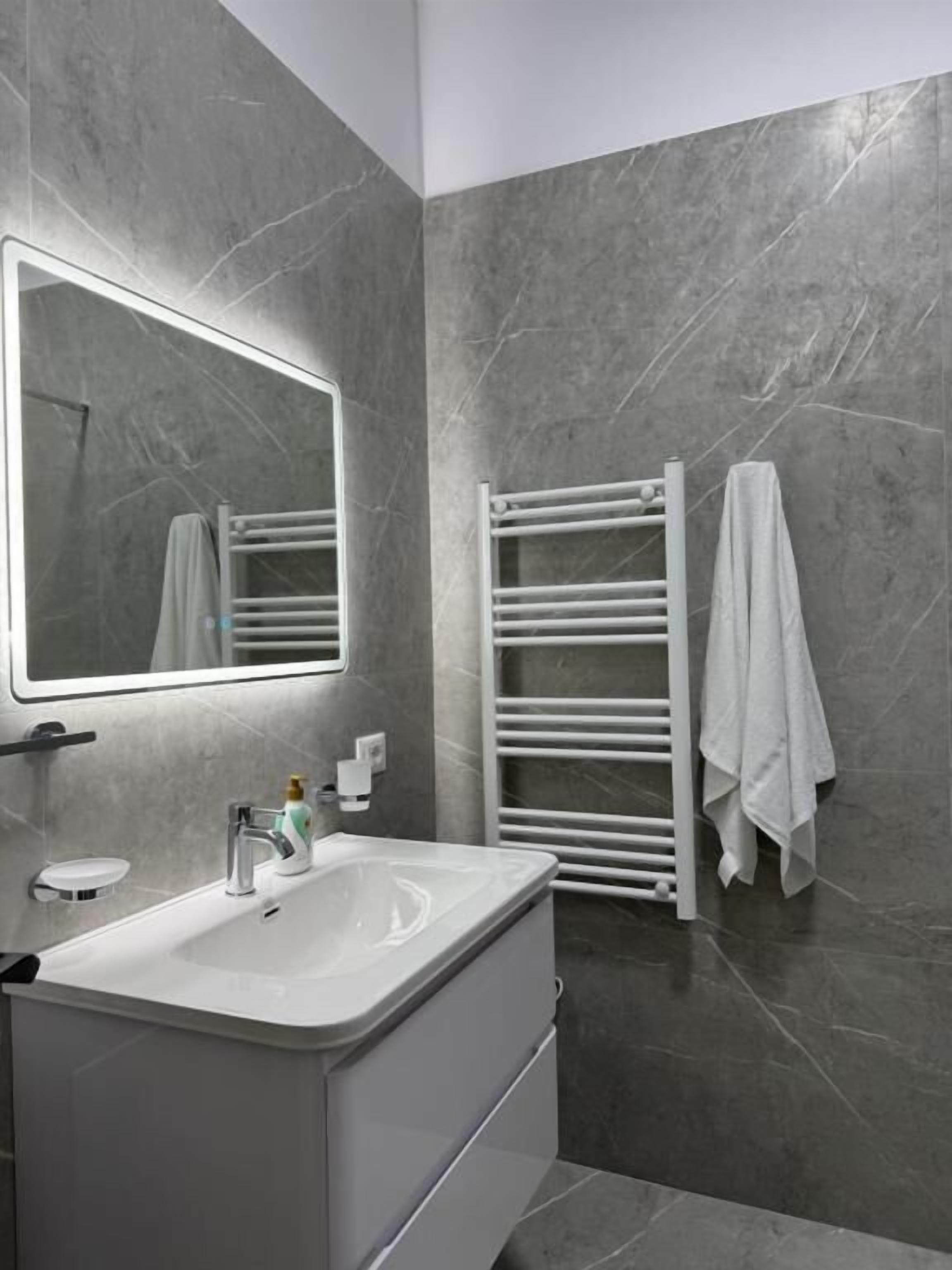 A modern bathroom with a large mirror, a white sink, and a towel rack.