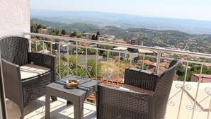 A balcony with wicker furniture, a small table, and a view of a town and hills. - Villa Duka (Kruje)