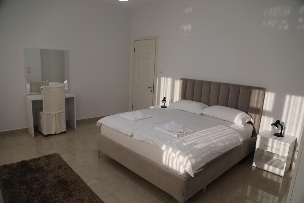 A bedroom with a bed, bedside table, nightstand, and a mirror.
