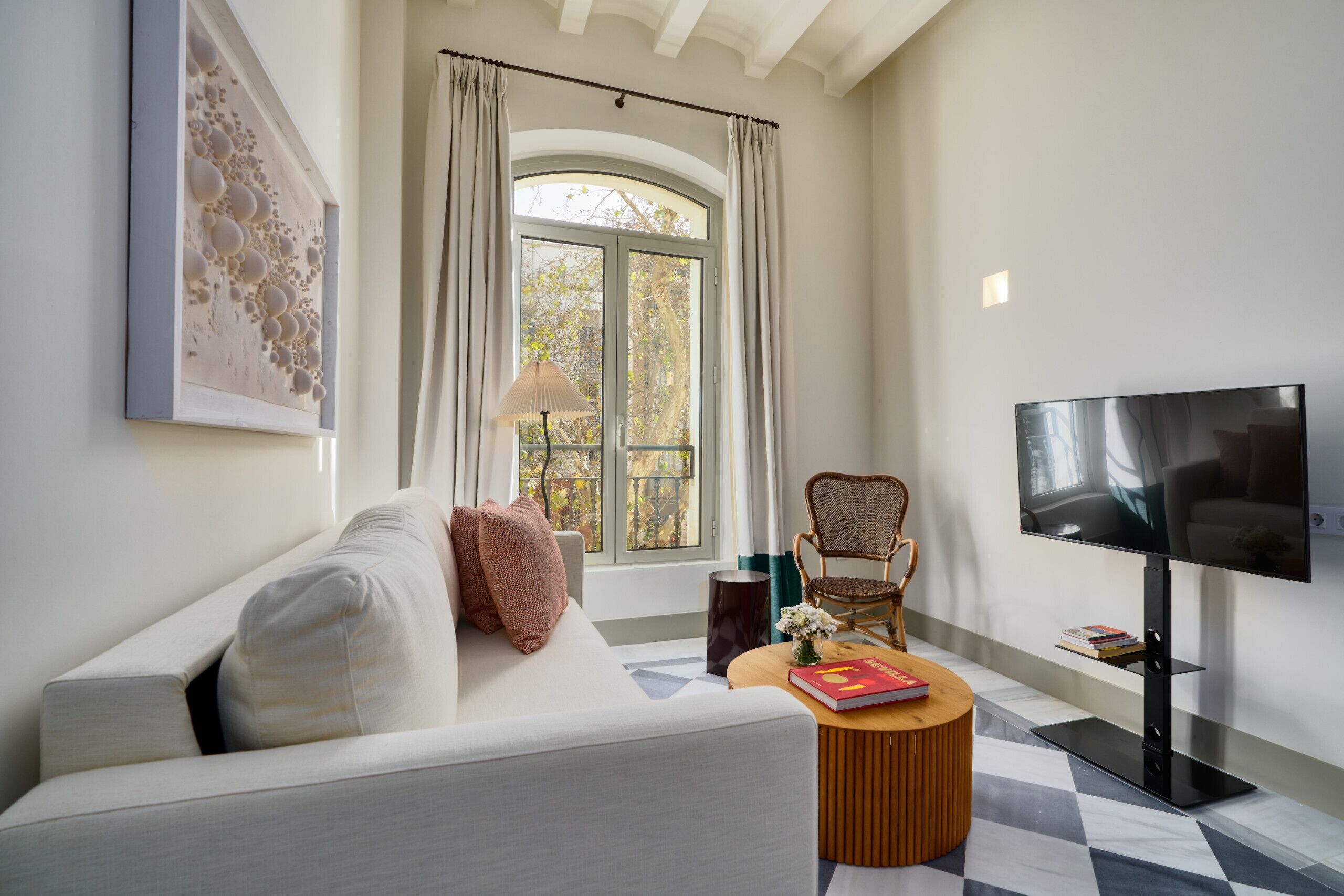 A modern living room with a sofa, a television, a round coffee table, and a window with curtains.