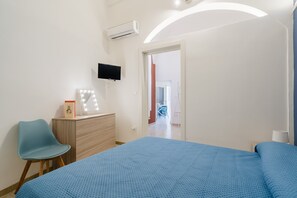 Un dormitorio con cama, cómoda, silla, televisor y aire acondicionado.
