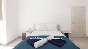 Habitación de hotel con una cama, dos mesitas de noche, una mesita auxiliar, una puerta y una ventana.